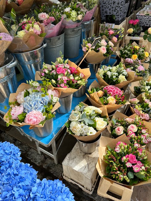 A vibrant display of freshly arranged flower bouquets on a table, featuring a variety of pastel and bright-colored blooms including pink roses, white and yellow daisies, blue hydrangeas, and green fol